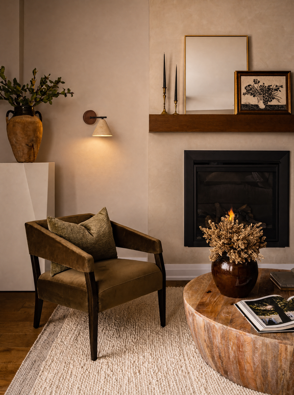 Fonte wall lamp lit above a velvet reading chair beside a fireplace