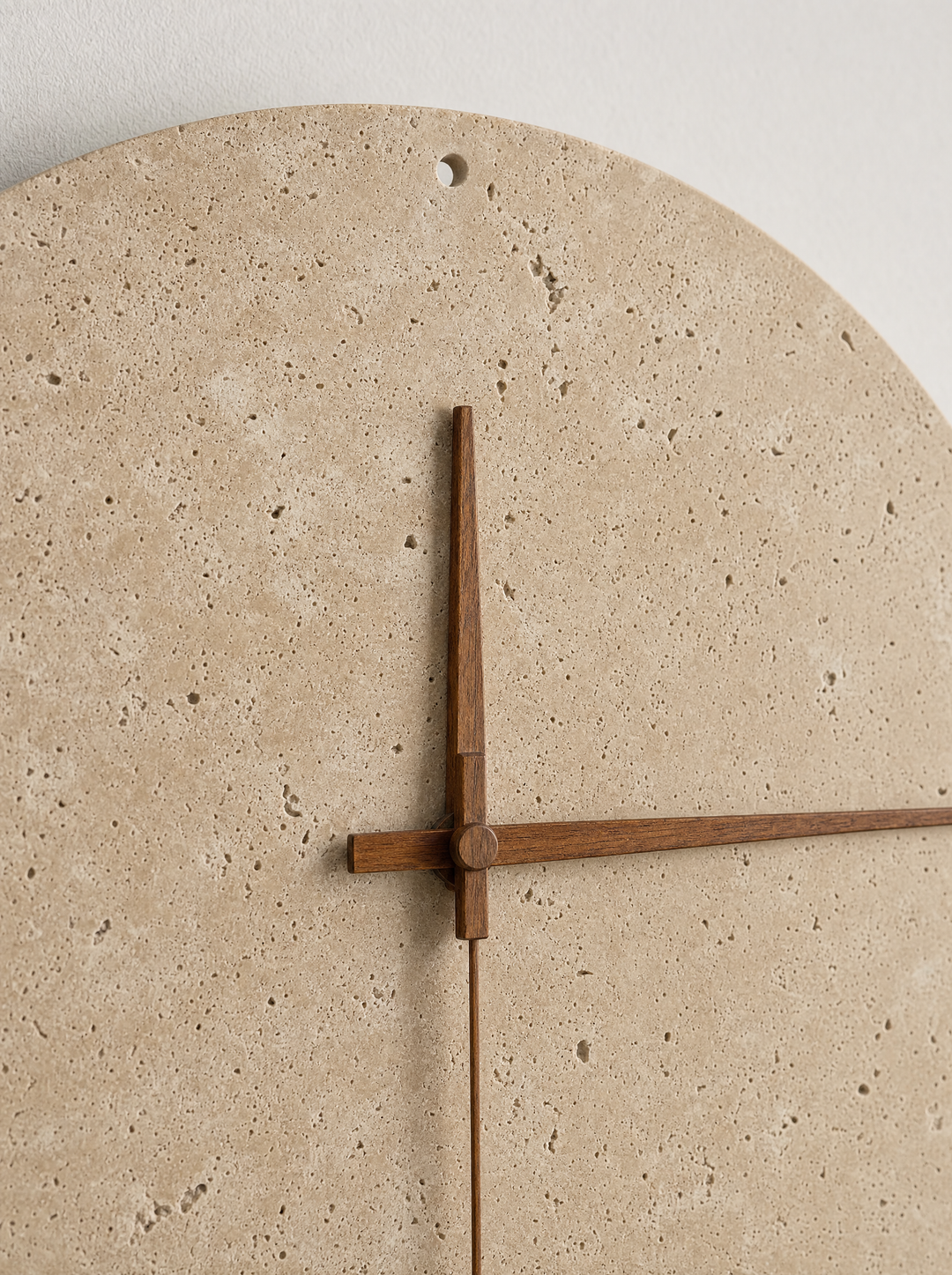 Close-up of Adagio travertine wall clock face showing the natural stone texture, walnut hands, and center spindle in the same walnut tone