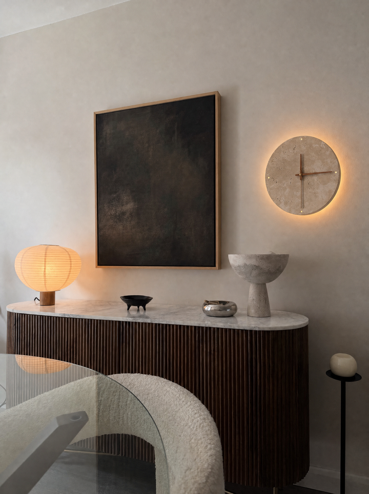 Adagio travertine wall clock above a console, its light washing the wall behind it, 23cm size