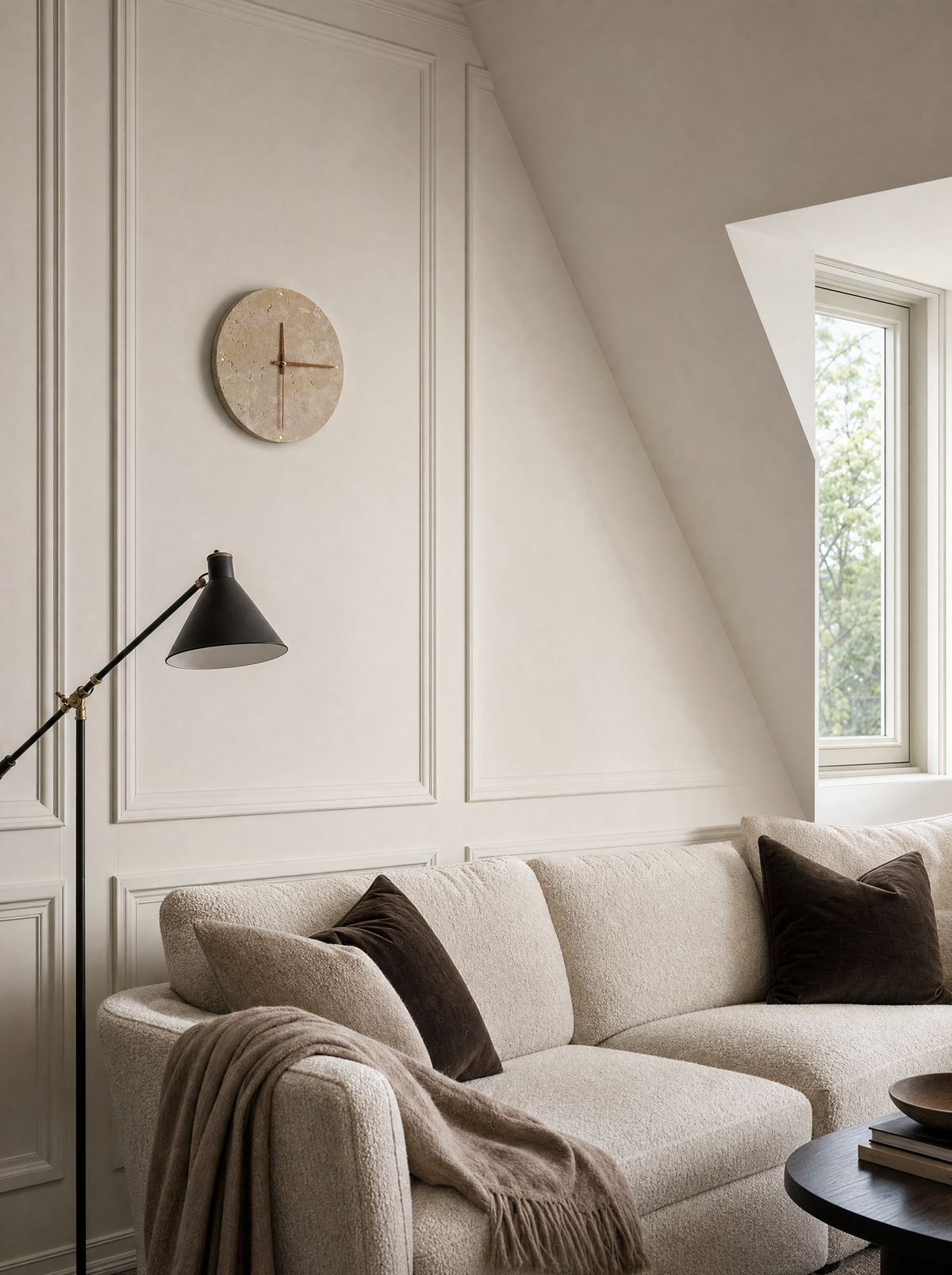 Adagio travertine wall clock, light off, mounted above a black cone floor lamp in an attic room