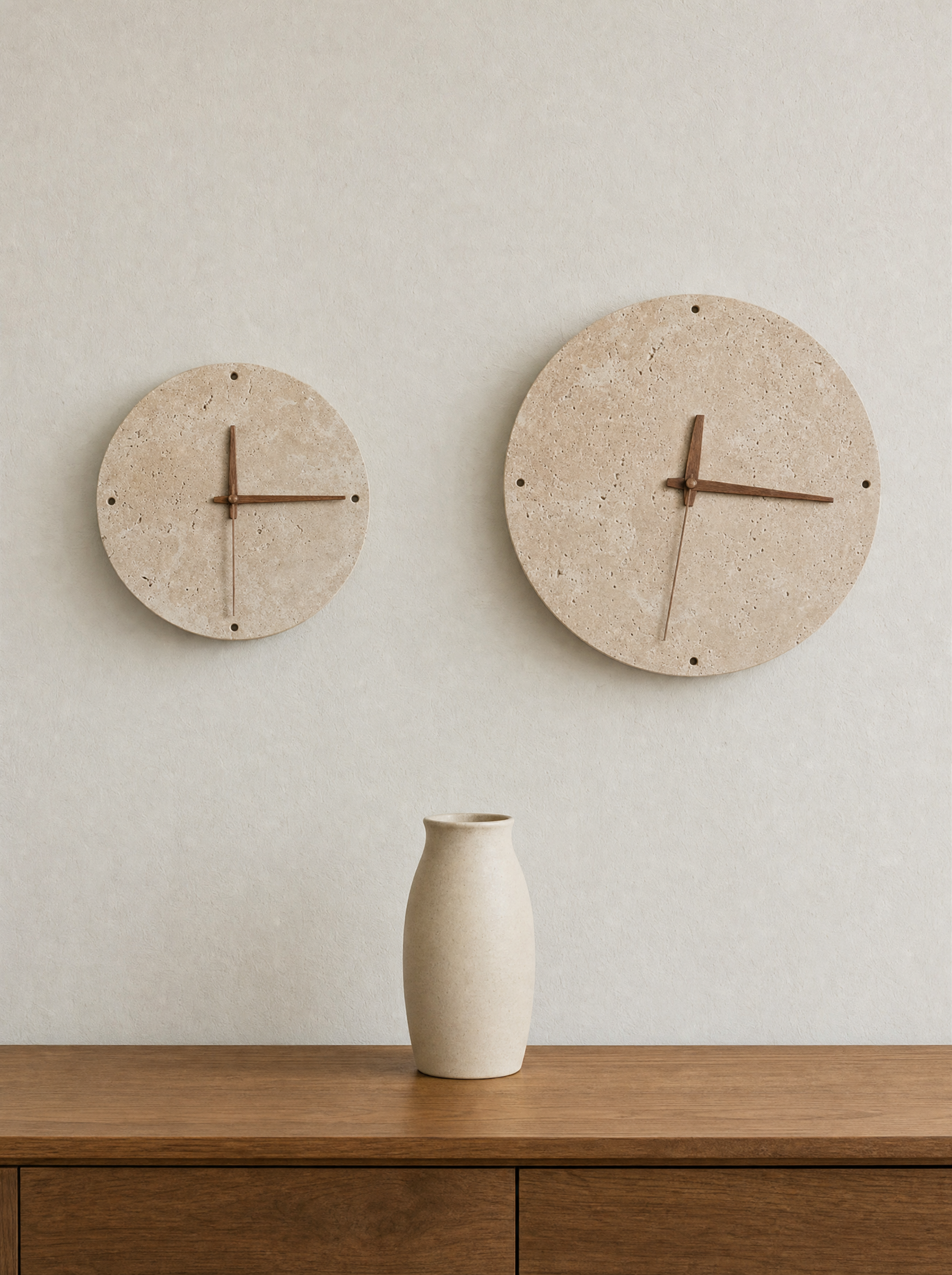Two sizes of Adagio travertine wall clock side by side on a plain wall, both lights off