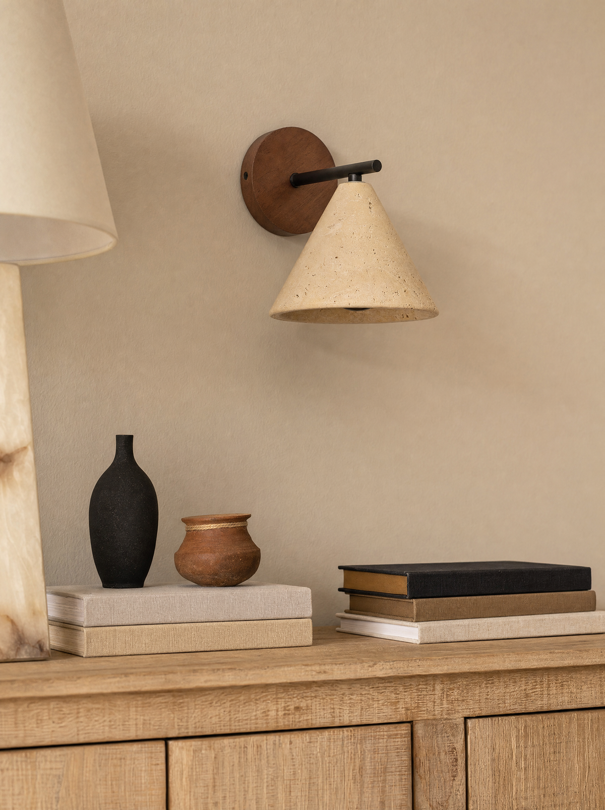 Close view of travertine stone pores on the Fonte shade, unlit, beside a dark ceramic vessel.