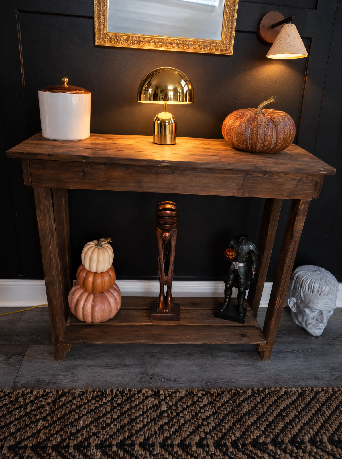 A wooden console set for Halloween under a gold mirror, with a lit gold Vespers lamp, a Fonte wall light and The Echo sculpture on the lower shelf