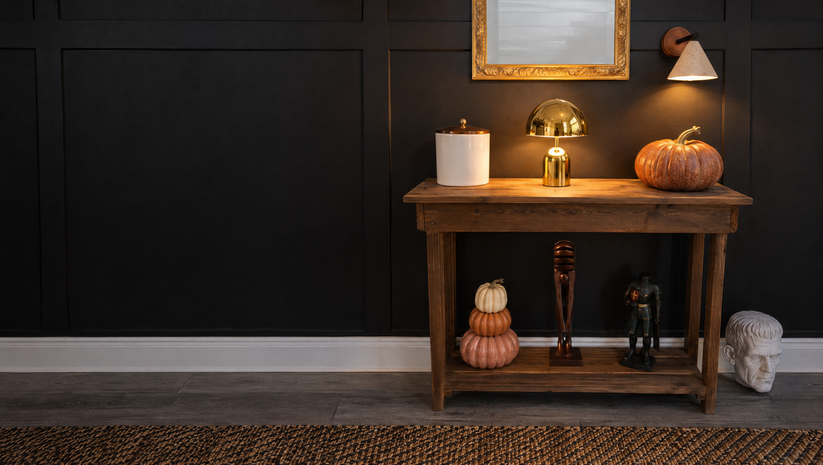 A dark paneled wall above a wooden console set for Halloween, with a lit gold Vespers lamp, a Fonte wall light and The Echo sculpture on the lower shelf