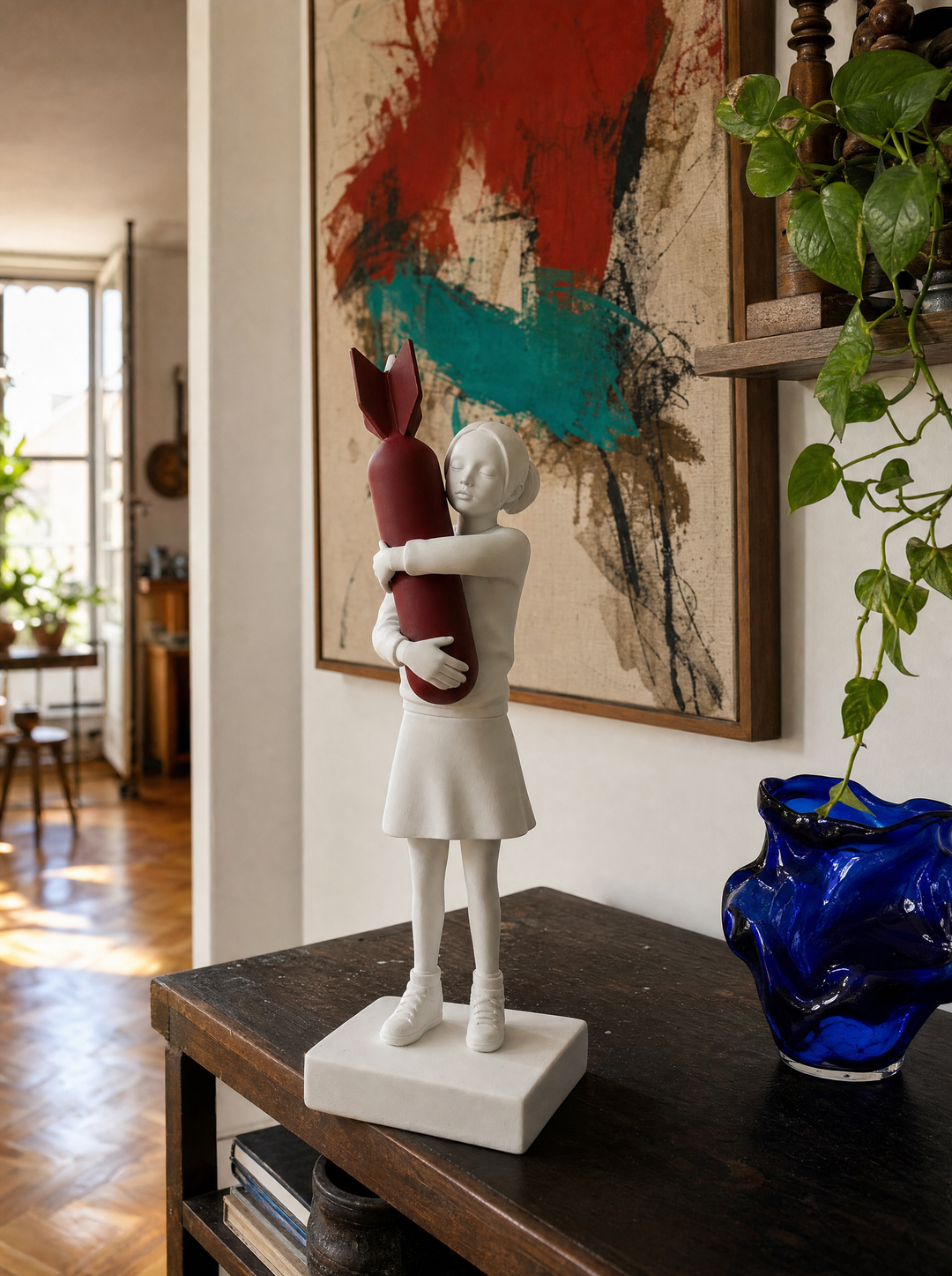 Disarm sculpture on a dark console before an abstract painting, blue glass vase