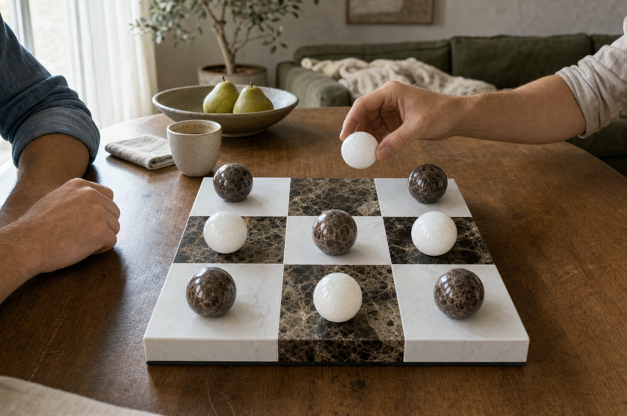 Two hands playing Lapilli, mid-game, on a wooden table in daylight.