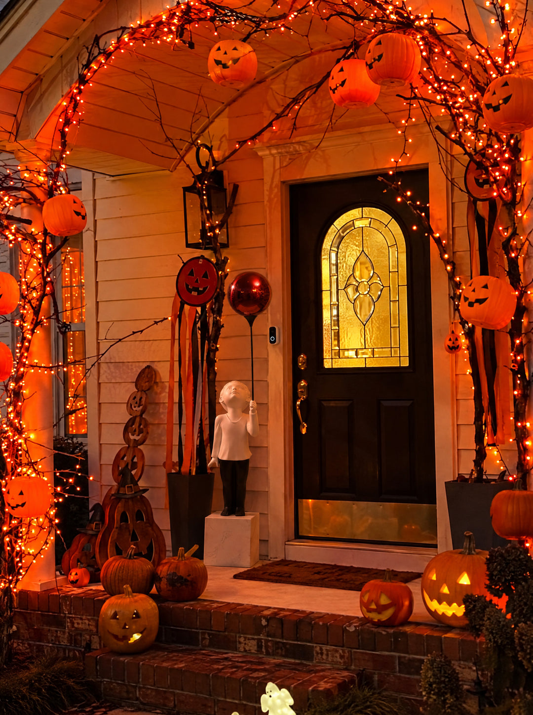 AeroCherub stands on a night porch, its red balloon held high against the warm orange of Halloween.