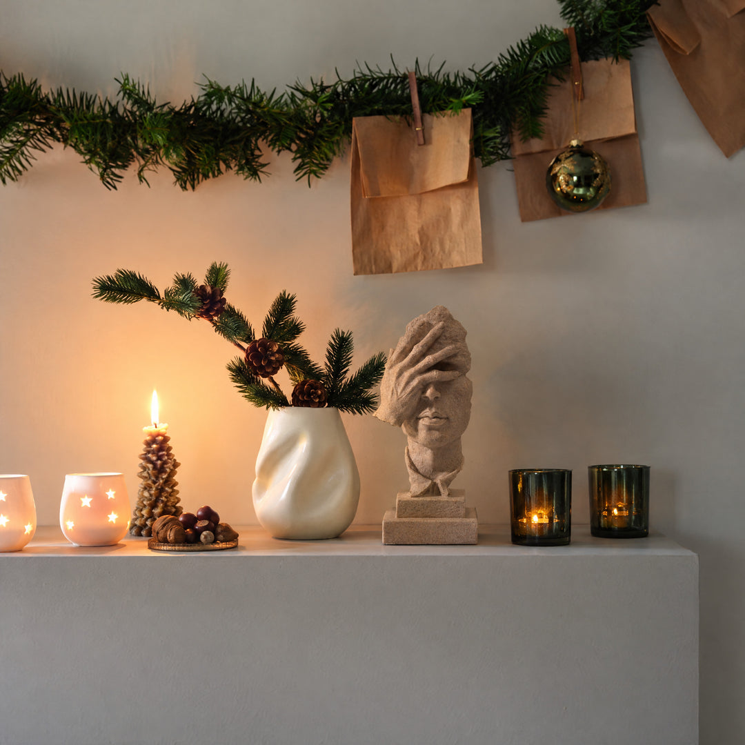 SilentMuse, a sculpted face in sand-beige stone, stands before a wall washed warm by one candle.