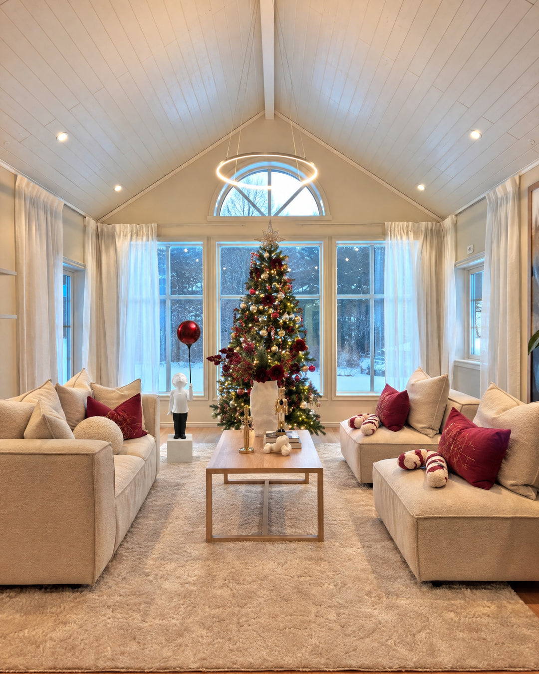AeroCherub holds its red balloon beside tall glass doors in a white, high-ceilinged room, with snowy pines outside and a red cushion nearby.