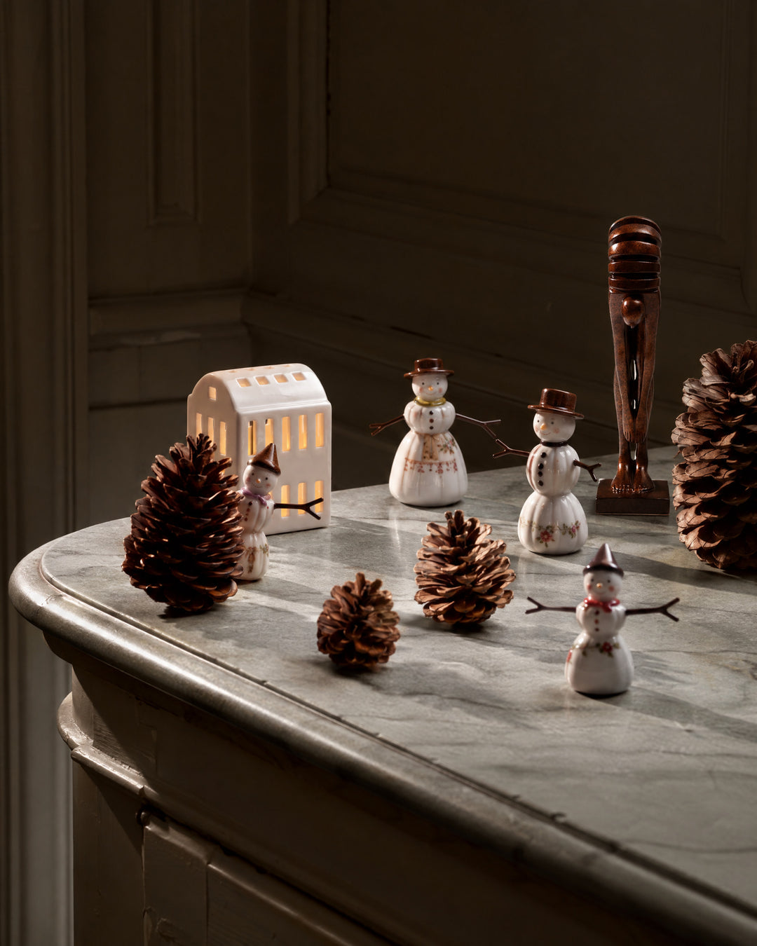 The Echo, a small figure of stacked discs, stands dark among white porcelain snowmen on a marble top.