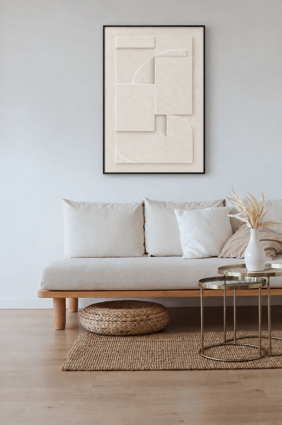 Chalk Rilievo wall relief above a low wooden sofa with cream cushions in a bright white living room, with brass nesting tables and a woven pouf