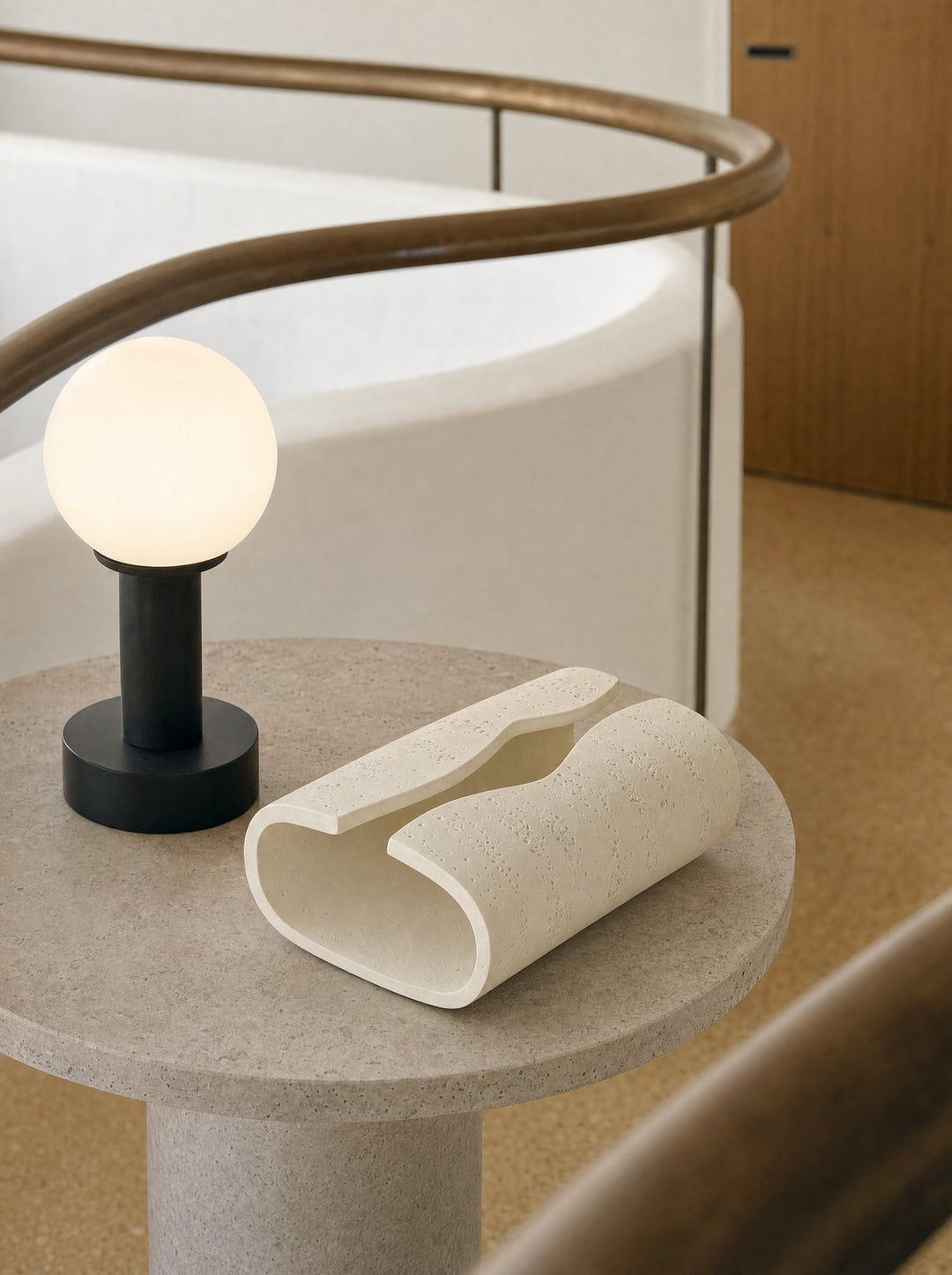 Volute ceramic tissue box beside a lit globe lamp on a round stone table